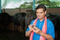 Indian milk dairy farmer busy using mobile phone at farm house - concept of technology, internet and small agri-business