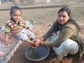 A indian mother washing her child feet with water child siting on cot both family face