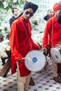 Indian musician guy drumming Dhol and wearing red Bandhgala and black Pheta at Indian wedding ceremony in Bangkok, Thailand