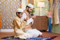 Indian Muslim father with kid doing namaz or praying during ramadan festival celebration at home - concept of ramzan