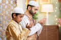 Indian Muslim father with kid doing namaz or praying during ramadan festival celebration at home - concept of ramzan