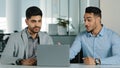 Indian oriental millennial male businessmen looking at laptop screen discussing project, satisfied with result of Royalty Free Stock Photo