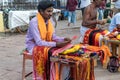 An Indian pilgrim in traditional attire selling colorful ribbons for Hindu rituals at the