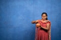 Indian poor girl saving money by placing coins on piggy bank or pot gullak by looking at camera - concept of financial