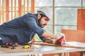 Indian professional bearded male engineer architect foreman labor worker carpenter wears safety helmet and gloves using wood