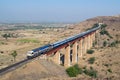 Indian railways long passenger train, exiting a tunnel to cross a tall railway bridge