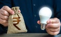 Indian rupee money bag and burning idea light bulb in the hands of a man. Royalty Free Stock Photo