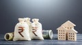 Indian rupee money bags and residential buildings figures. Investments in real estate. Mortgage loan. Financing the construction