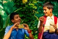 Indian school boy eating sandwich and his friend with backpack sits on table and eating an apple in park Royalty Free Stock Photo