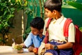 Indian school boy writing on notepad doing homework , looking concentration . His friend with backpack sits on table and Royalty Free Stock Photo