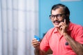 Indian senior man talking on mobile phone by holding tablets in hand at home - concept of telemedicine, elderly health Royalty Free Stock Photo