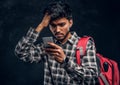 Indian student with a backpack forgot about something very important and with a frustrated look looks at his smartphone.