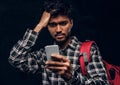 Indian student with a backpack forgot about something very important and with a frustrated look looks at his smartphone.