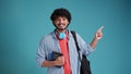 Indian student guy isolated on blue background with backpack on shoulders points with hand on place for text