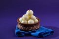 Indian Sweet or Dessert - Rasgulla, Famous Bengali sweet in clay bowl with blue napkin on violet background