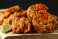 Indian takeaway food, spicy onion bhajis served with chili yoghurt dip and lime wedges on wooden board Royalty Free Stock Photo