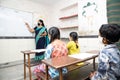 Indian teacher and students wearing face masks maintaining social distancing study in classroom back at school during covid19