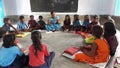 Indian teachers sit on the ground in whole groups and discuss with the child by showing the plant