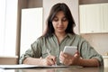 Indian girl holding phone online learn in mobile app write notes at home office.