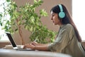 Indian teen girl student wear headphones watching online class making notes.