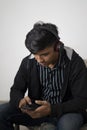 Indian teenager boy black jacket with headphone sitting on floor at home. handsome guy looking at smartphone sctreen Royalty Free Stock Photo