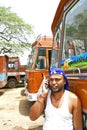 Indian truck driver talking on his mobile phone with trucks parked on his back.