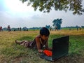 an indian village boy lying on green grass background during online working on laptop in India January 2020 Royalty Free Stock Photo