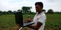 An indian village farmer operating laptop computer system in agriculture background