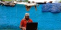 An indian village man operating laptop computer system seating in front of blue wall at home Royalty Free Stock Photo