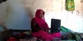 An indian village woman operating laptop computer system seating at cot