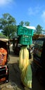 An Indian village woman walking with heavy vegetable container on road