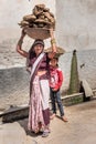 Indian woman and girl carrying basin with cow dung cakes on their heads in Nandgaon. India