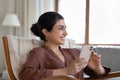 Indian woman looks aside rest on armchair with cellphone indoor Royalty Free Stock Photo