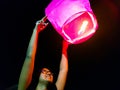 An indian woman releasing a lighted paper hot air balloon in sky lantern festival