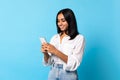 Indian woman scrolling via smartphone chatting online on blue background