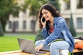 Indian woman student using computer and talking on phone outdoor Royalty Free Stock Photo