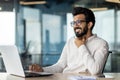 Indian young male businessman suffering from severe sore throat, sitting in office at desk, working on laptop and Royalty Free Stock Photo