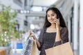 Indian young smiling woman standing in a shopping mall, holding paper shopping bags, talking on the phone and looking at Royalty Free Stock Photo