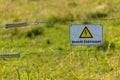 Indicating label `Vorsicht Elektrozaun` caution electric fence on metal bare wires in front of a meadow