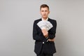 Indifferent young business man in classic black suit holding lots bunch of dollars banknotes, cash money isolated on