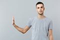 Indifferent young man in casual clothes looking camera, showing stop gesture with palm aside isolated on grey wall