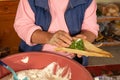 Indigenous woman preparing tamales with masa, stuffed with vegetables, covered by a corn leaf, traditional Mexican food