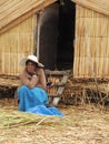 An indigenous woman sitting by a straw house at Uros floating islands in Lake Titicaca in Peru
