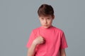 Indignant displeased teenager boy points at herself asks why me, dressed in casual pink t shirt, poses against gray background