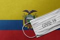 Face Medical Surgical White Mask with COVID-19 inscription lying on Ecuador National Flag. Coronavirus in Ecuador