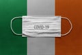 Face Medical Surgical White Mask with COVID-19 inscription lying on Ireland Flag. Coronavirus in Ireland Royalty Free Stock Photo