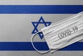 Face Medical Surgical White Mask with COVID-19 inscription lying on Israel National Flag. Coronavirus in Israel