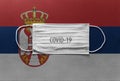 Face Medical Surgical White Mask with COVID-19 inscription lying on Serbia National Flag. Coronavirus in Serbia