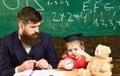 Individual lesson concept. Boy, child on calm face holds alarm clock while teacher talk to kid. Teacher with beard Royalty Free Stock Photo