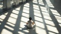 An individual meditates in a sunlit modern space, casting a pattern of shadows and light.
